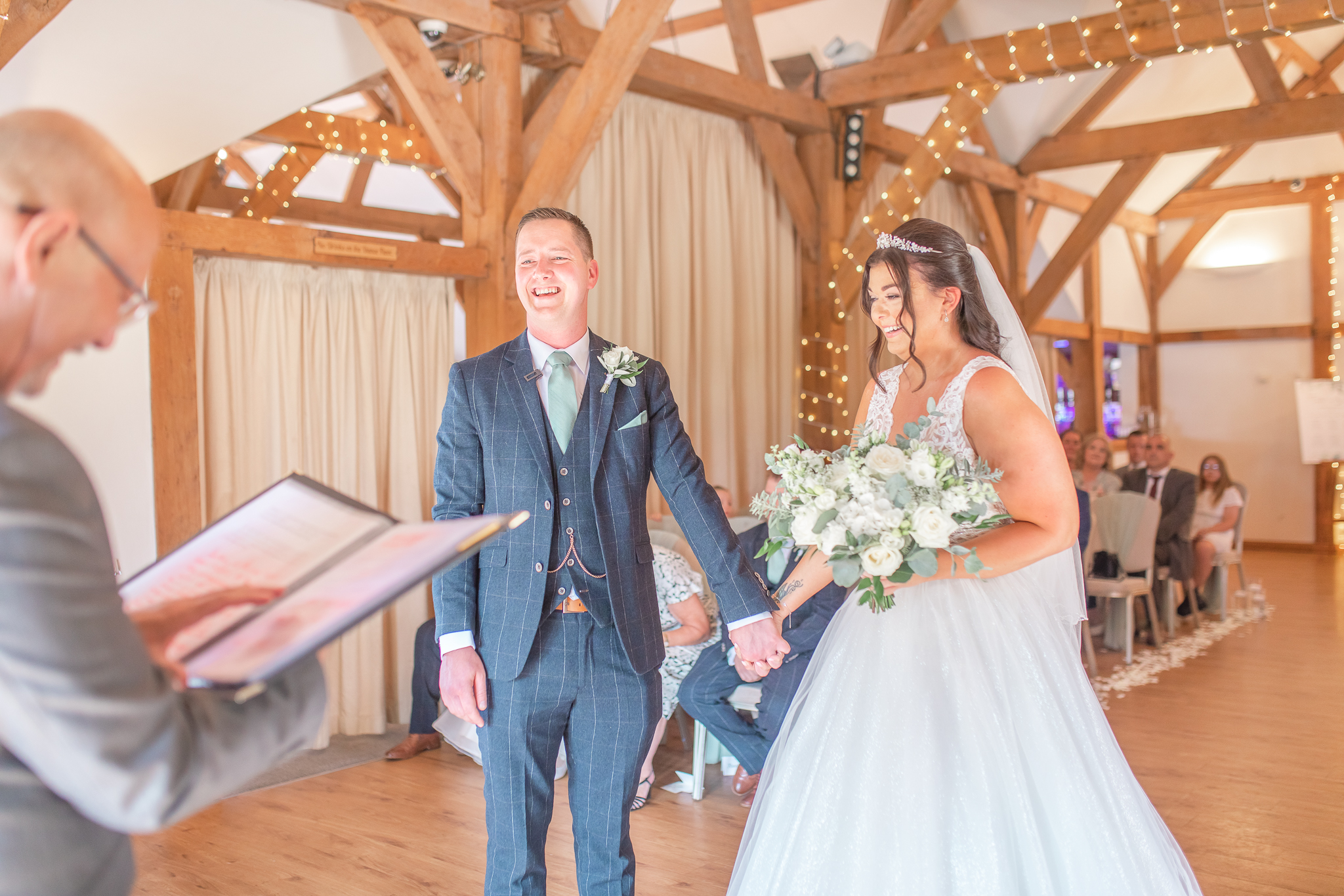 Aimee and Ant holding hands and laughing during their wedding ceremony at Sandhole Oak Wedding Barn in Cheshire