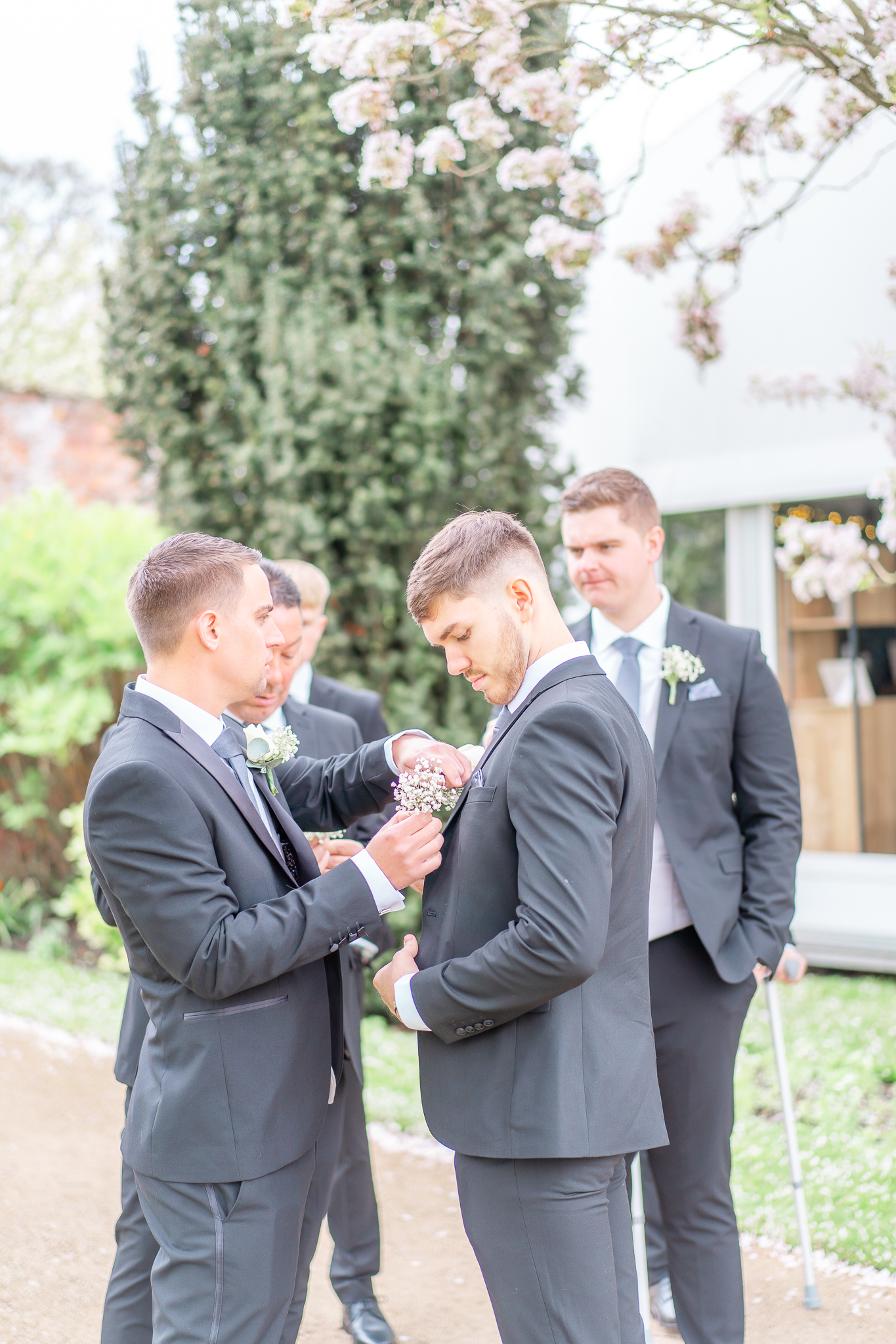 Candid moment of Spencer putting his groomsmen's buttonholes on at Combermere Abbey 