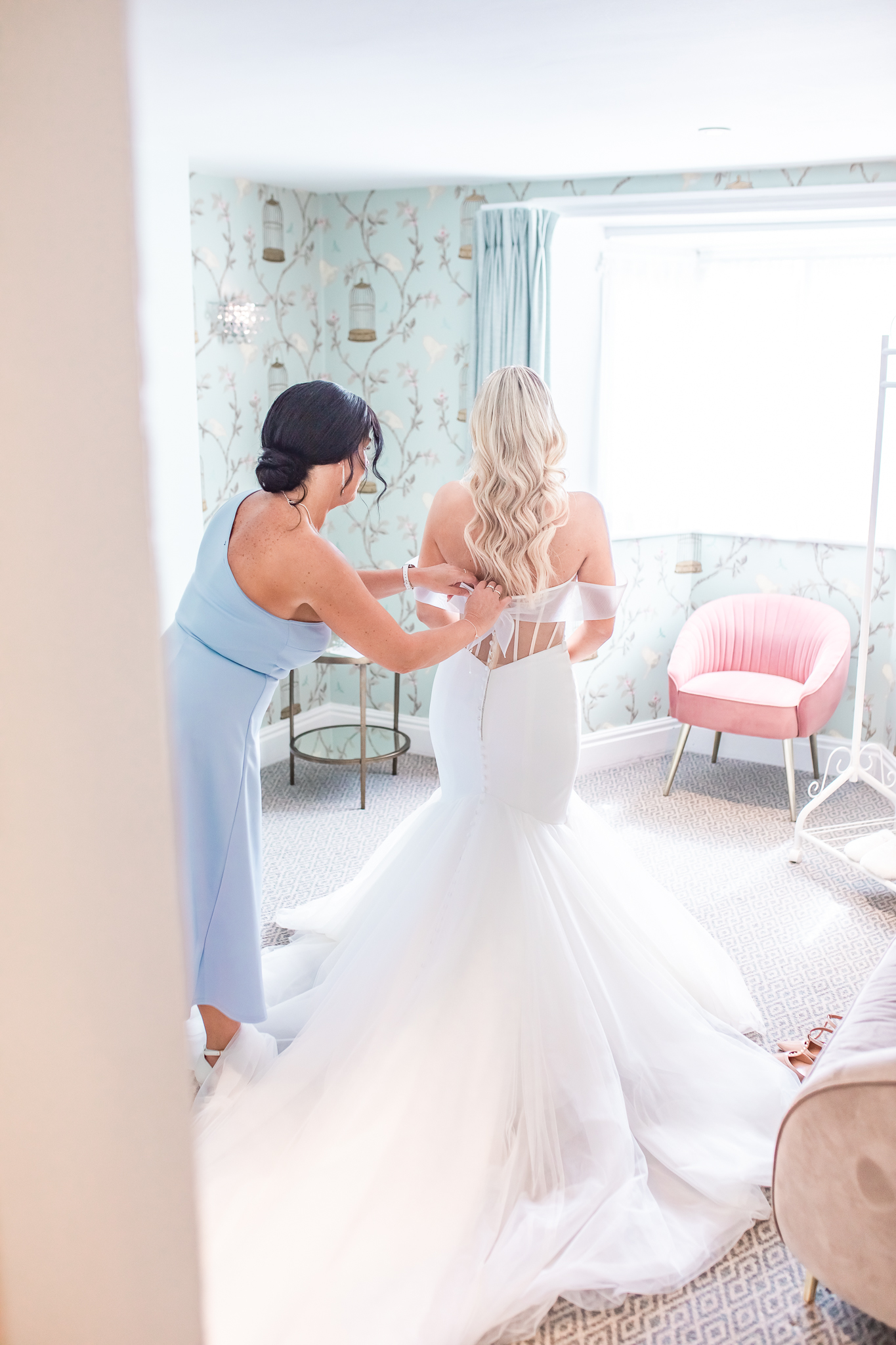 Mother of the bride helping bride, Kelsey with her wedding dress at Keepers Cottage at Combermere Abbey in Cheshire taken by Cheshire wedding photographer, Sophie Siddons