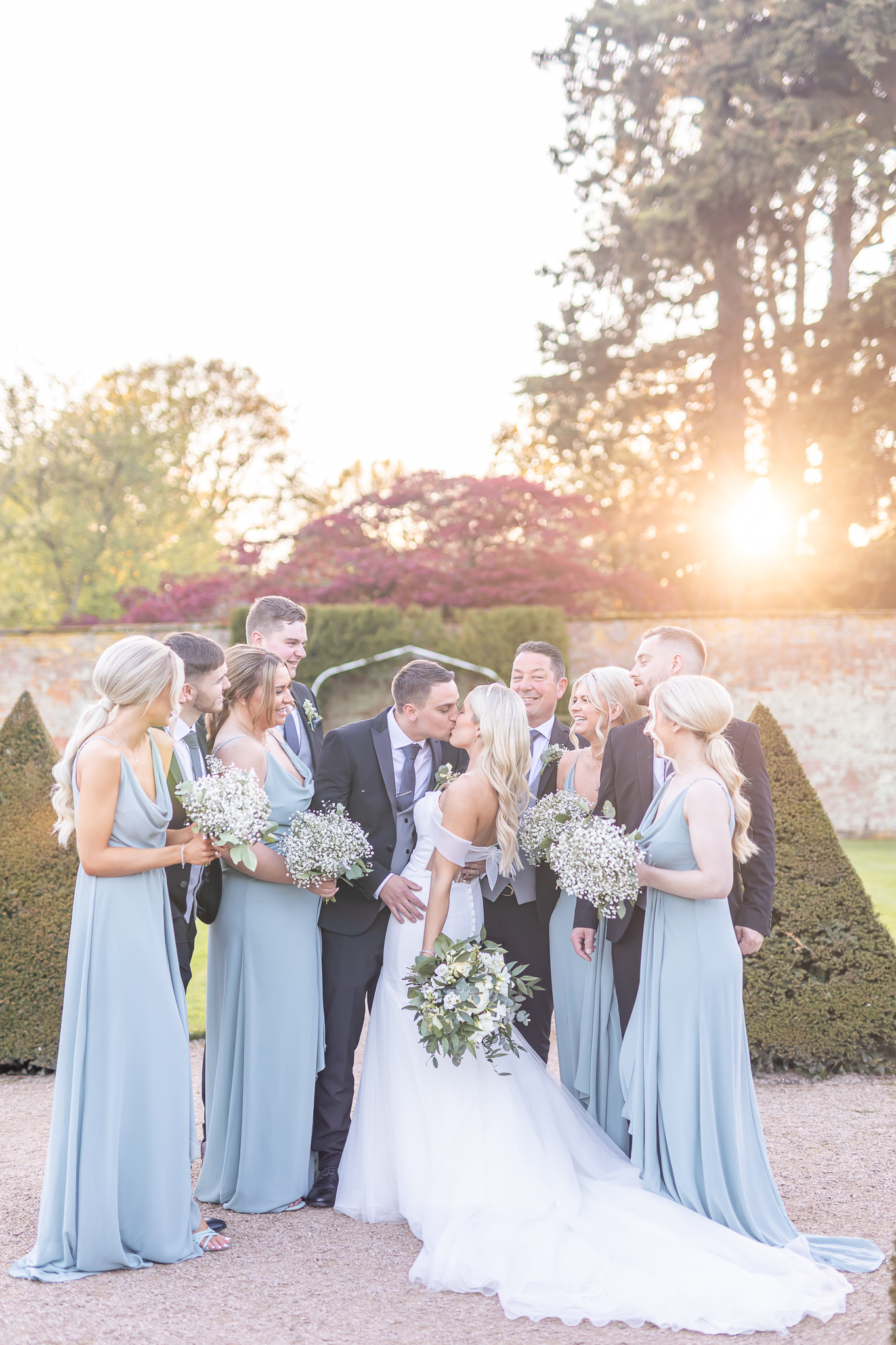 Bride and groom sharing a kiss surrounded by friends and family during sunset at Combermere Abbey in Cheshire