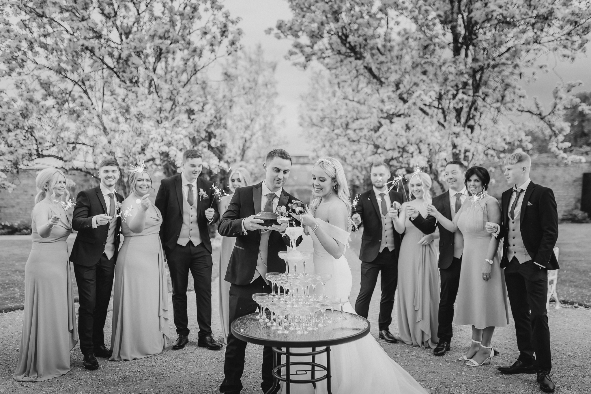 Kelsey and Spencer pouring Champagne with their bridal party surrounding them with sparklers at Combermere Abbey in Cheshire