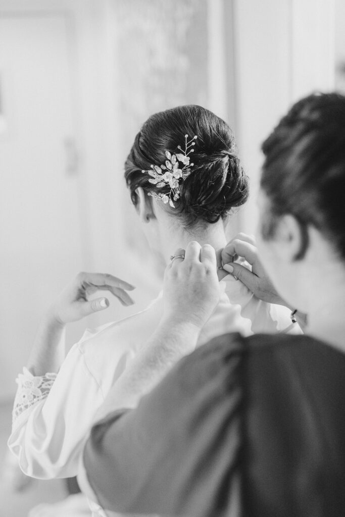 Candid moment of a bridesmaid putting on the brides necklace in the bridal suit at The Ashes Wedding Barns in Staffordshire taken by Cheshire wedding photographer Sophie Siddons