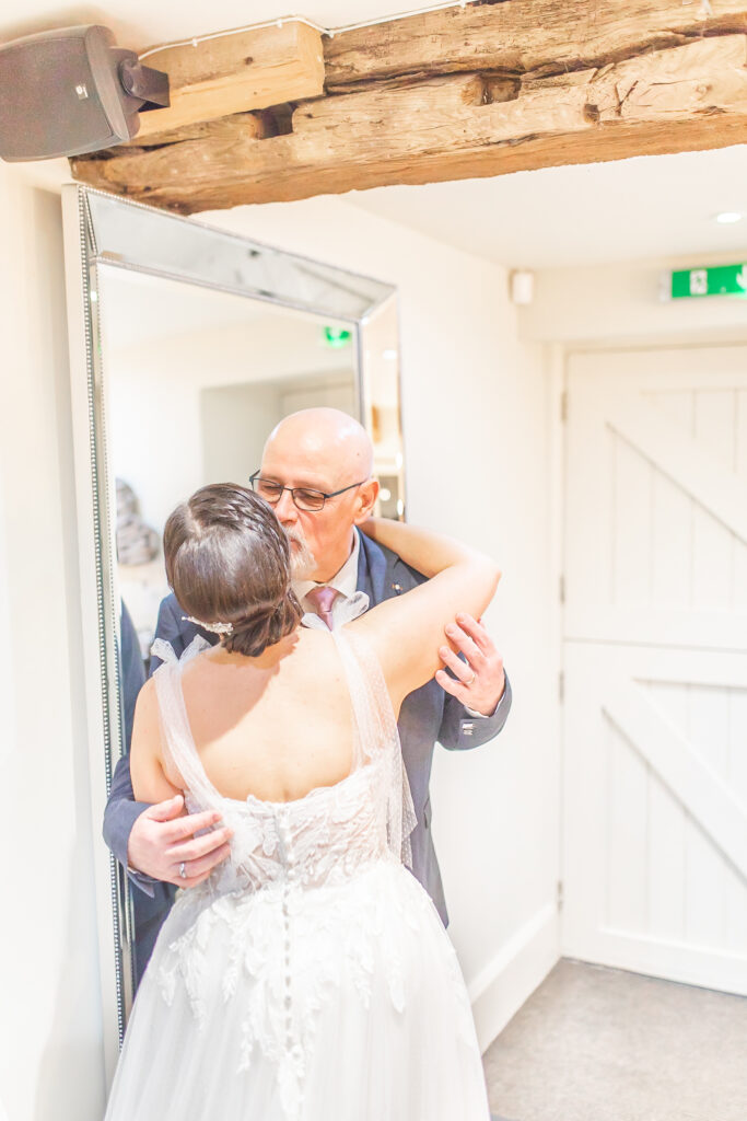 Candid moment of Father of the bride hugging the bride in the bridal suit at The Ashes Wedding Barns in Staffordshire taken by Cheshire wedding photographer Sophie Siddons