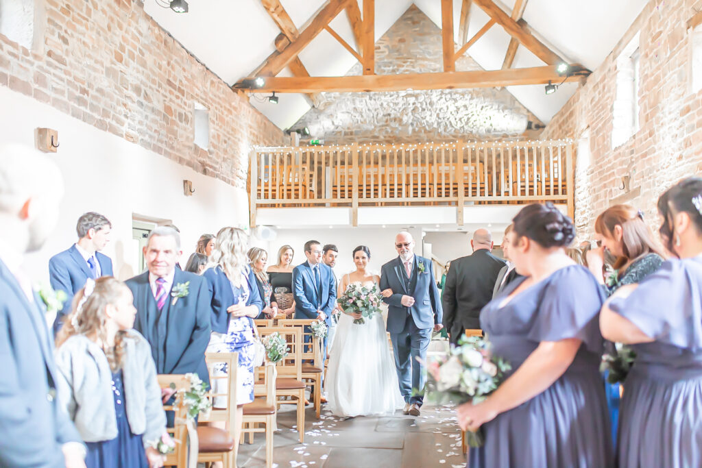 Bride and father of the bride walking arm in arm down the aisle at The Ashes Wedding Barns in Staffordshire