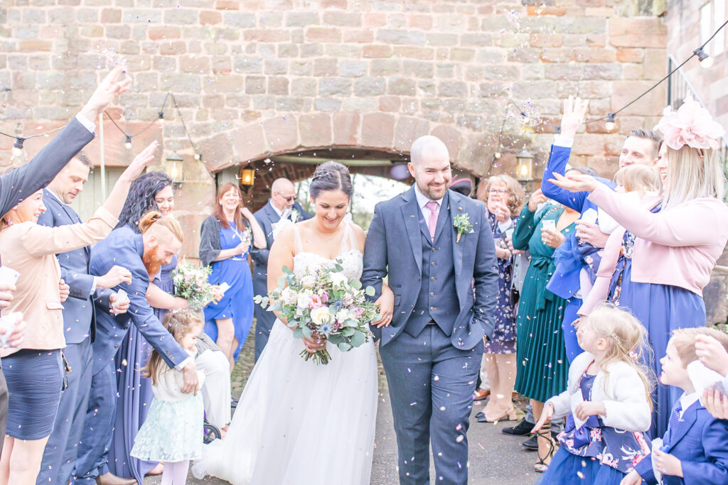 Bride and groom arm in arm surrounded by their guests throwing confetti at The Ashes Wedding Barns in Staffordshire