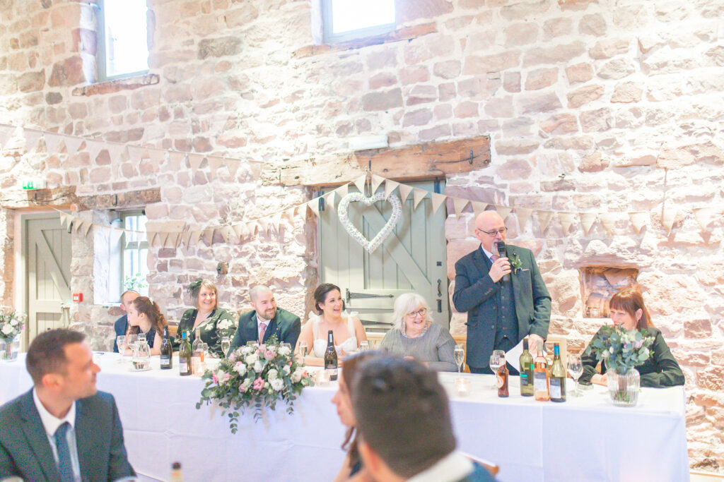 Wide shot of the top table at The Ashes wedding Barns during father of the brides speech, everyone is laughing.
