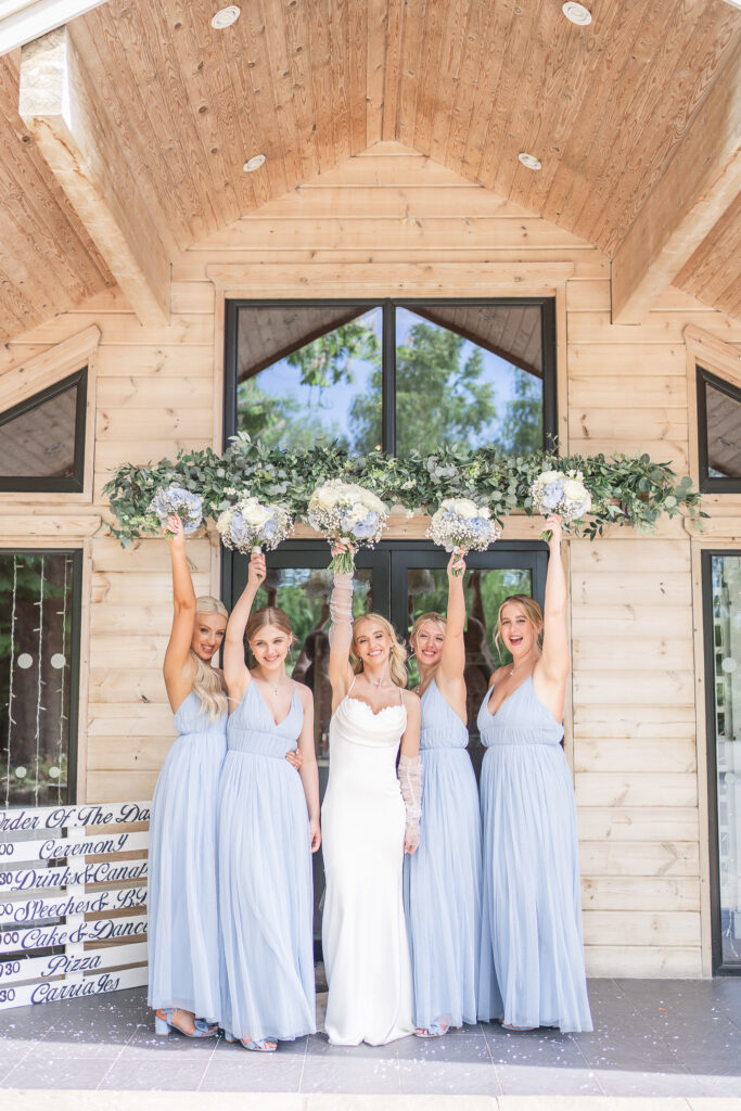 Bride and four bridesmaids holding up their bouquets outside of Styal Lodge wedding venue in Cheshire