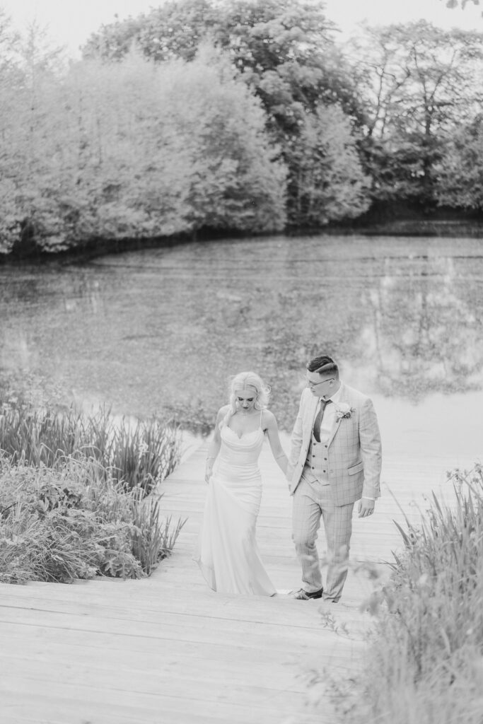 Bride and groom walking hand in hand in front of a lake